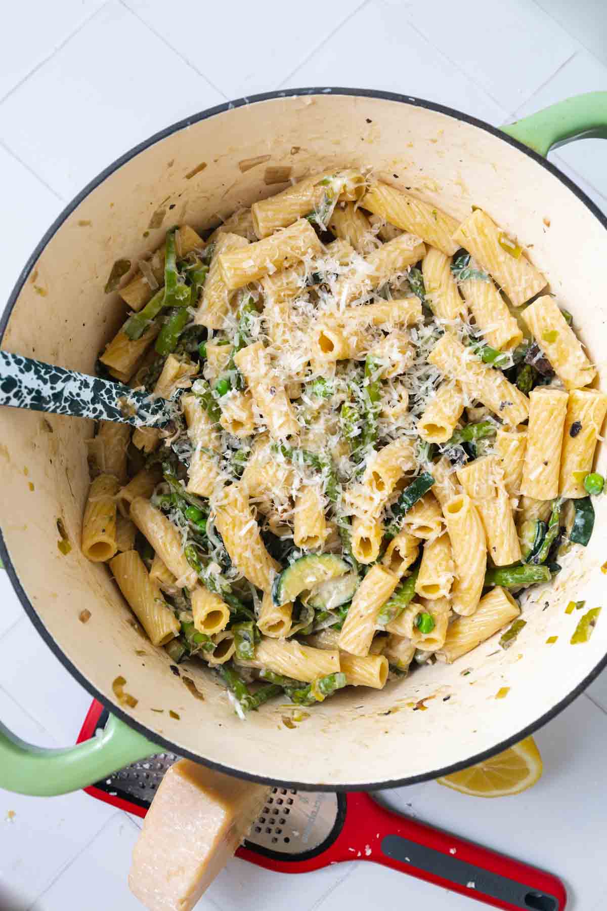 Large white Dutch oven filled with rigatoni, vegetables, and shredded Parmesan.