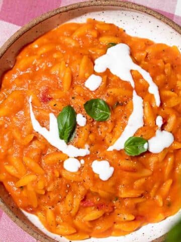 Brown-rimmed white bowl filled with red pepper orzo and a swirl of coconut cream.