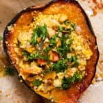 Half of a roasted acorn squash stuffed with couscous and topped with parsley on a piece of parchment paper.