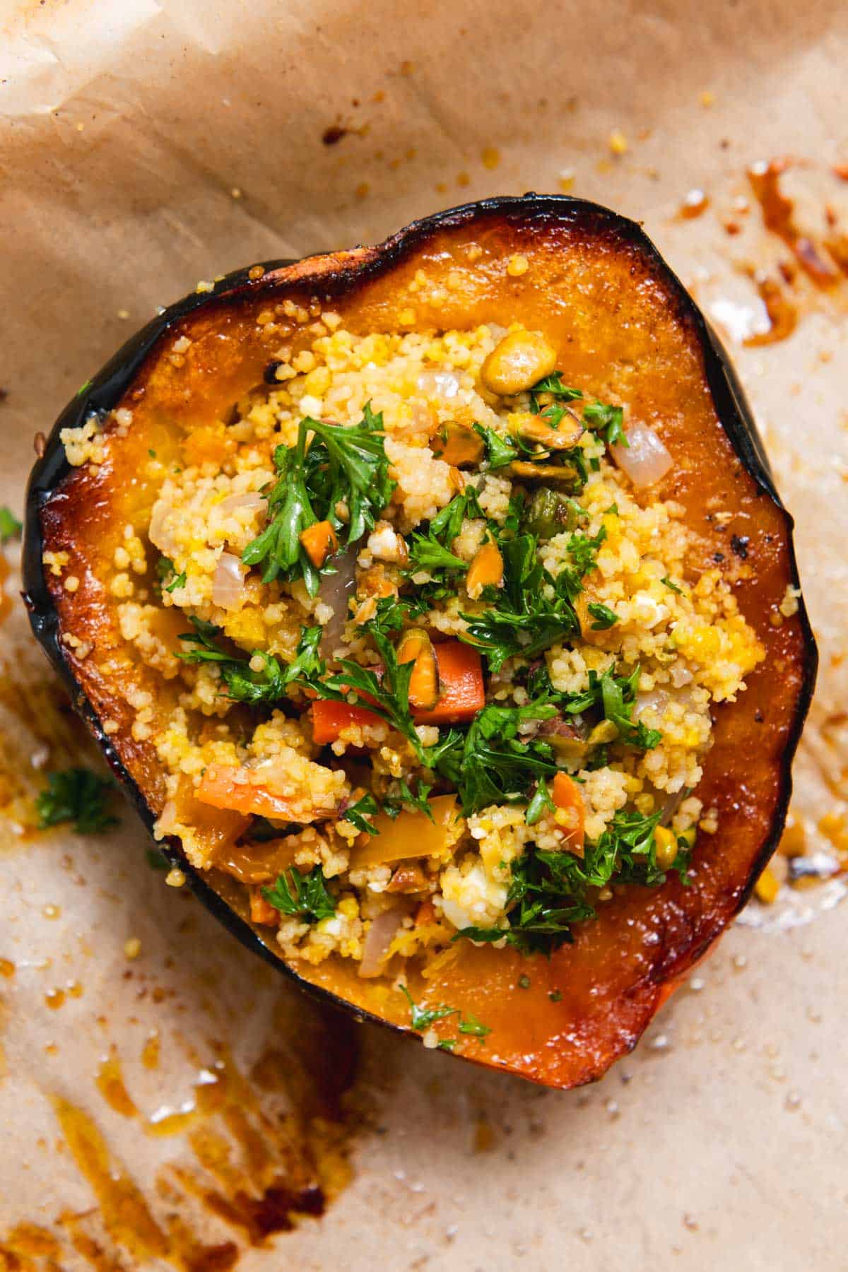 Half of a roasted acorn squash stuffed with couscous and topped with parsley on a piece of parchment paper.