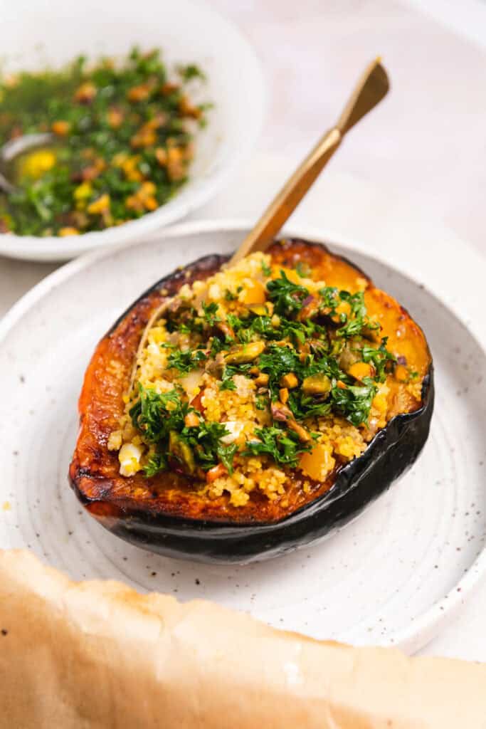 Side view of stuffed squash on a white plate with a gold fork resting in the squash.
