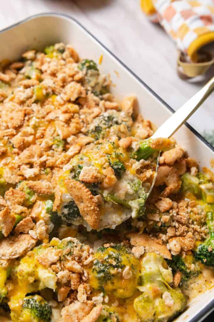 Gold serving spoon lifting a portion of broccoli cheese casserole out of the baking dish.