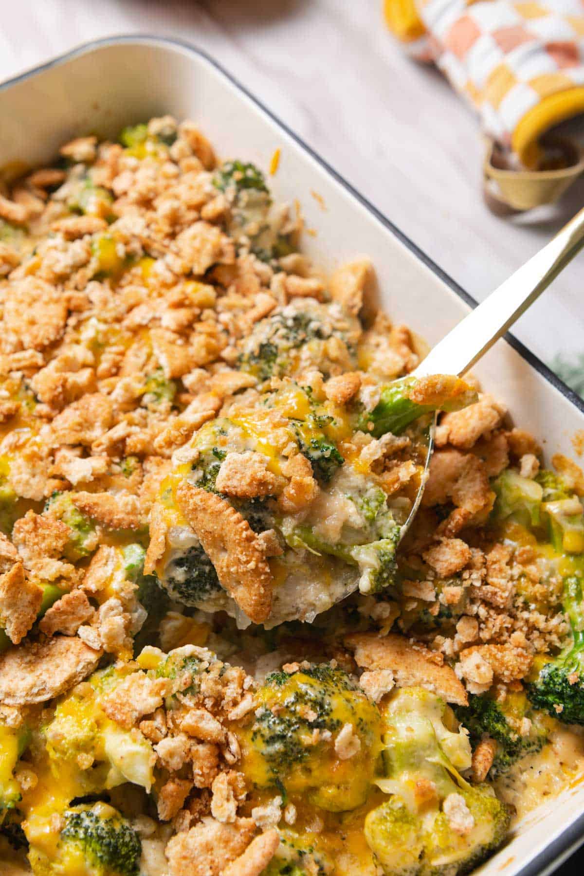 Gold serving spoon lifting a portion of broccoli cheese casserole out of the baking dish.