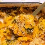 Gold serving spoon lifting a portion of butternut squash casserole out of the baking dish.