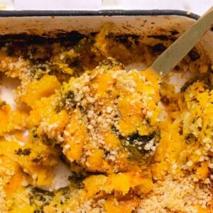 Gold serving spoon lifting a portion of butternut squash casserole out of the baking dish.