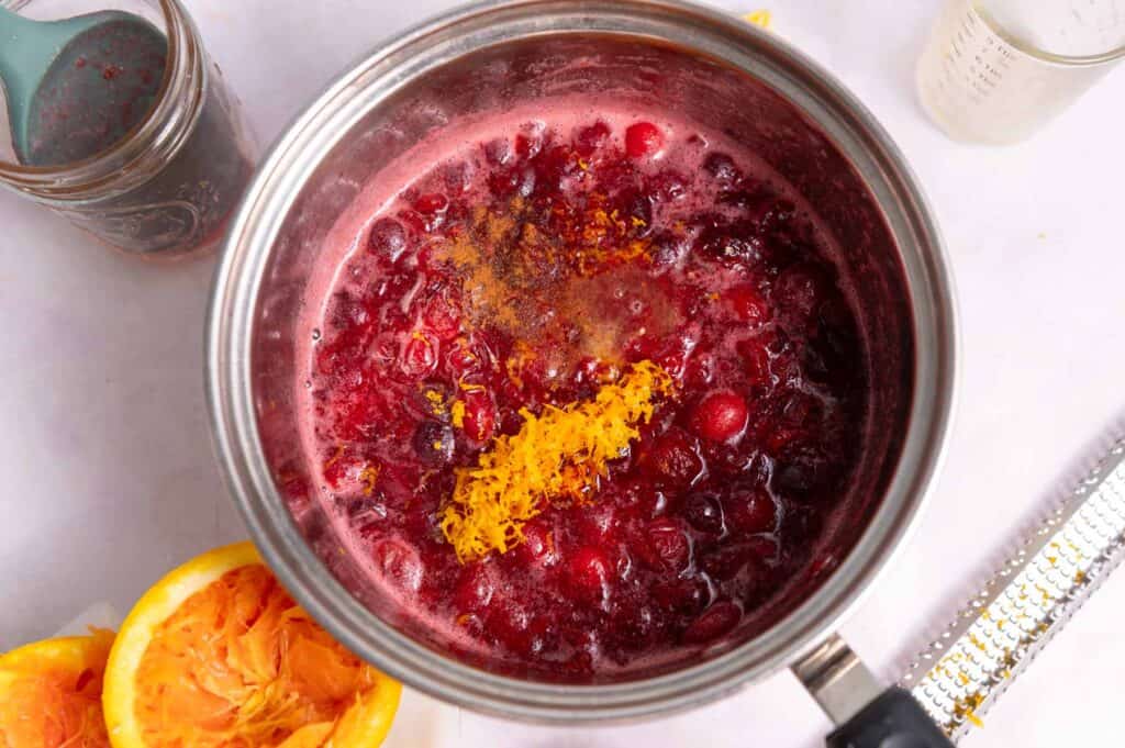 Jammy cranberries and orange zest in a silver pot.
