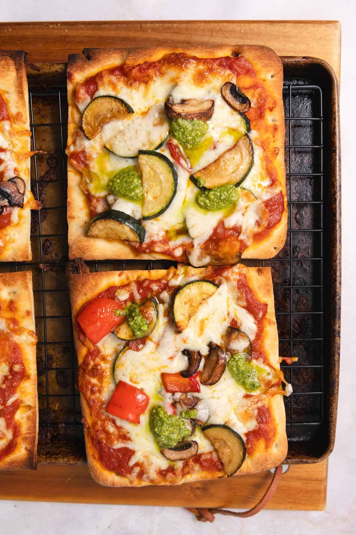 Two squares of veggie pizza on a wire cooling rack on a sheet pan.