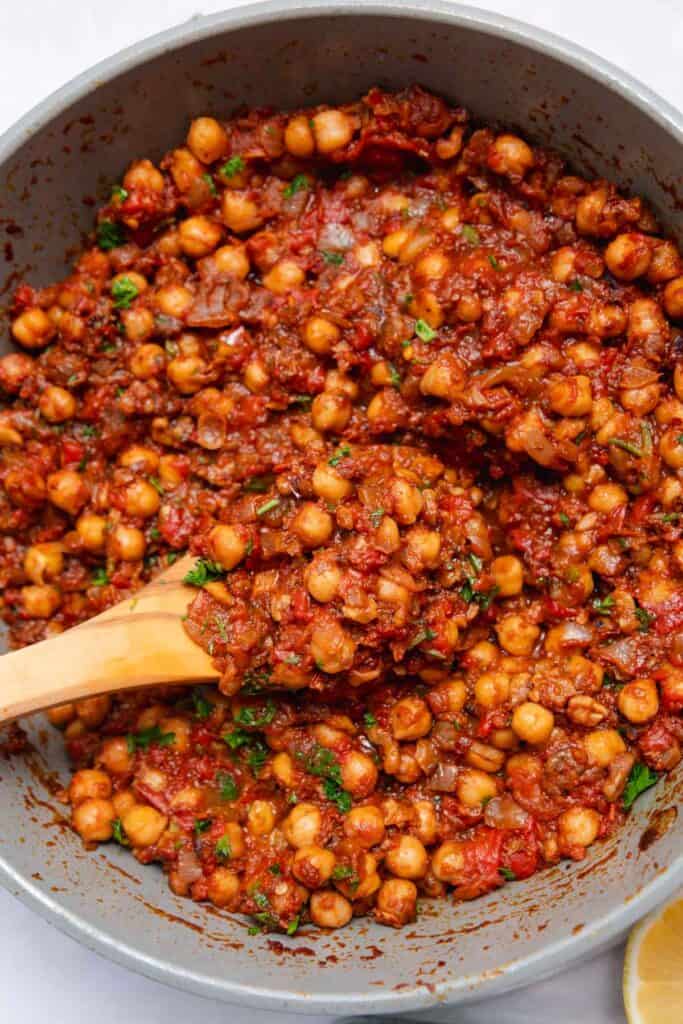 Wooden spatula lifting a scoop of stewed chickpeas out of a gray pot.