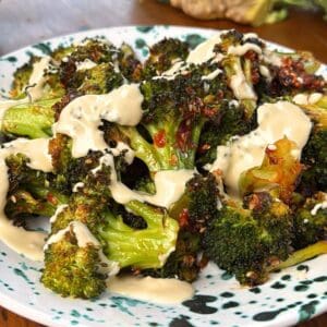 Blue-speckled bowl filled with roasted broccoli drizzle with tahini dressing.