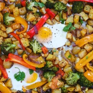 Close up of two fried eggs nestled among peppers, broccoli, onions, and potatoes.