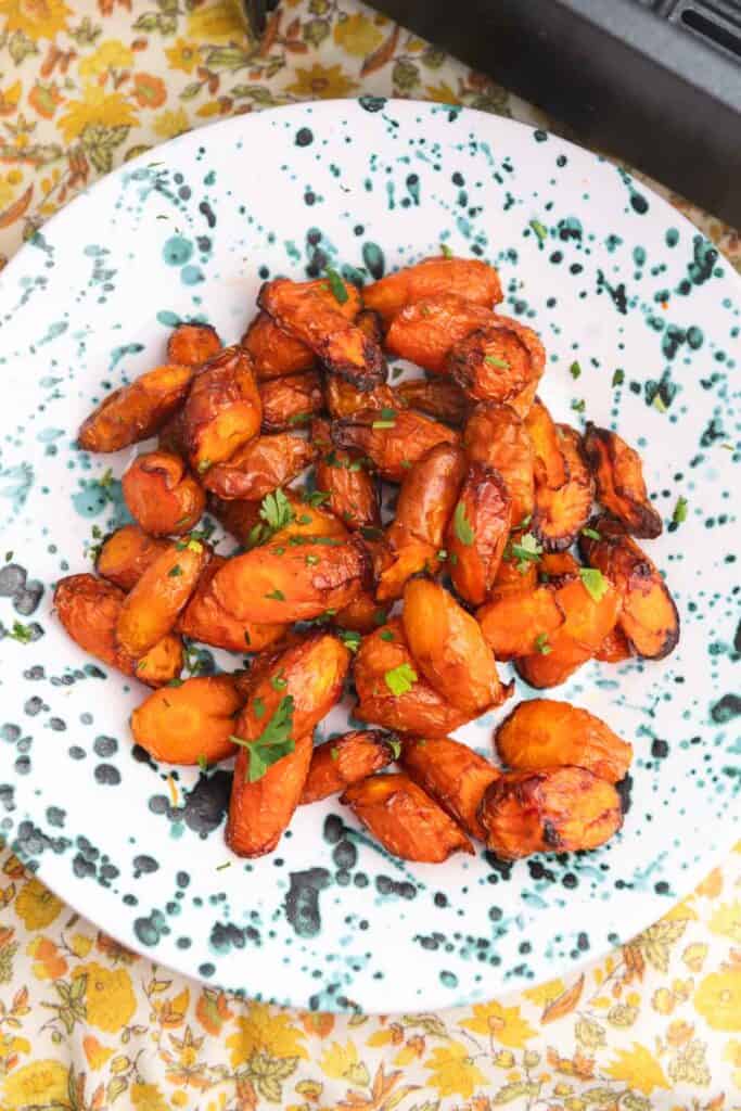 Carrot coins in a blue speckled bowl on a yellow floral cloth.