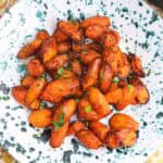 Carrot coins in a blue speckled bowl on a yellow floral cloth.