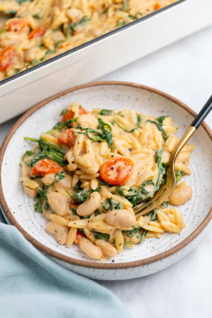 Brown-rimmed white bowl filled with a serving of orzo with a gold fork resting in the bowl.