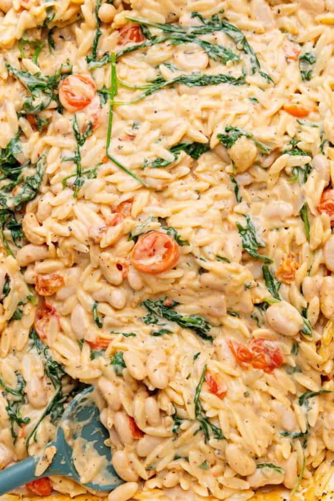 Close up of creamy orzo with tomatoes and arugula.