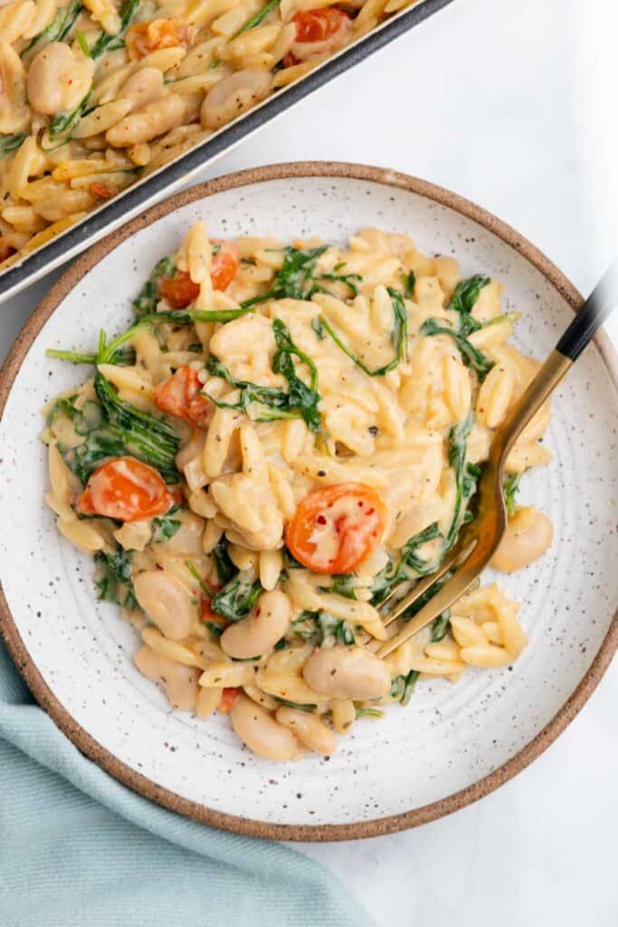 Brown-rimmed white bowl filled with a serving of orzo with a gold fork resting in the bowl.