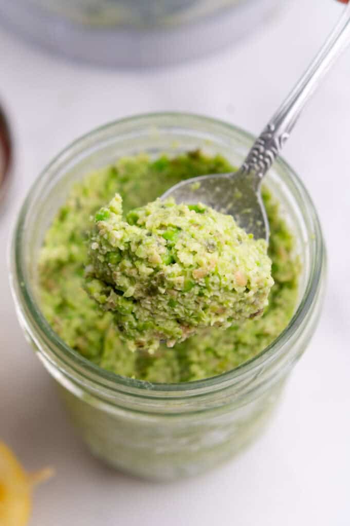 Spoon lifting green edamame dip out of a glass jar.