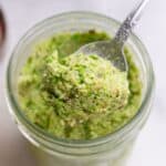 Spoon lifting green edamame dip out of a glass jar.