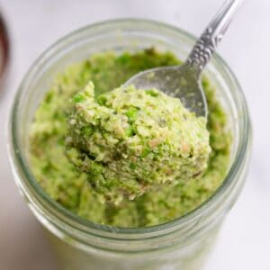 Spoon lifting green edamame dip out of a glass jar.