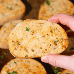 Hand holding up a slice of golden garlic toast.
