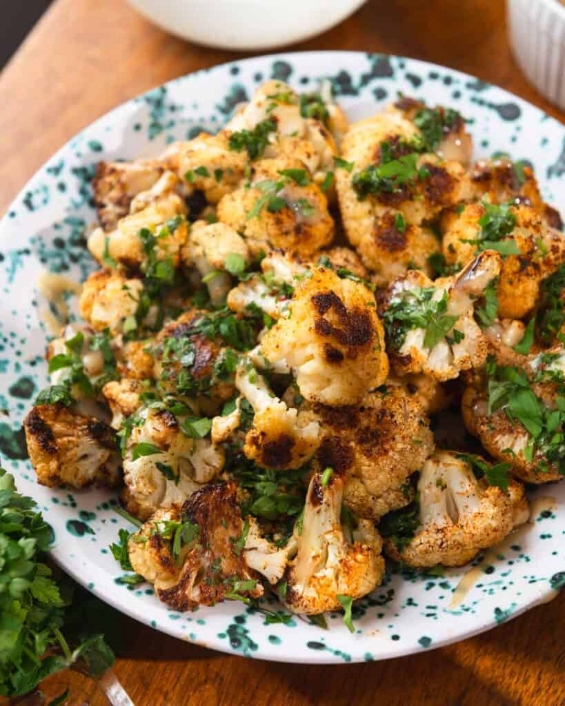 Roasted cauliflower topped with chopped herbs on a blue speckled plate.