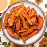Sweet potato wedges piled on a brown-rimmed white plate on a colorful flower tablecloth.