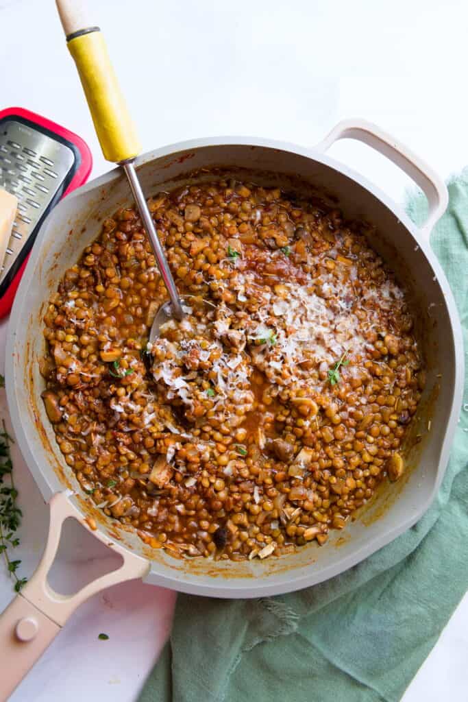 Gray skillet filled with braised lentils with a yellow-handled slotted spoon resting in the lentils.