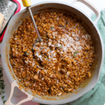 Gray skillet filled with braised lentils with a yellow-handled slotted spoon resting in the lentils.