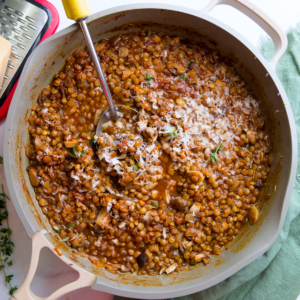 Gray skillet filled with braised lentils with a yellow-handled slotted spoon resting in the lentils.