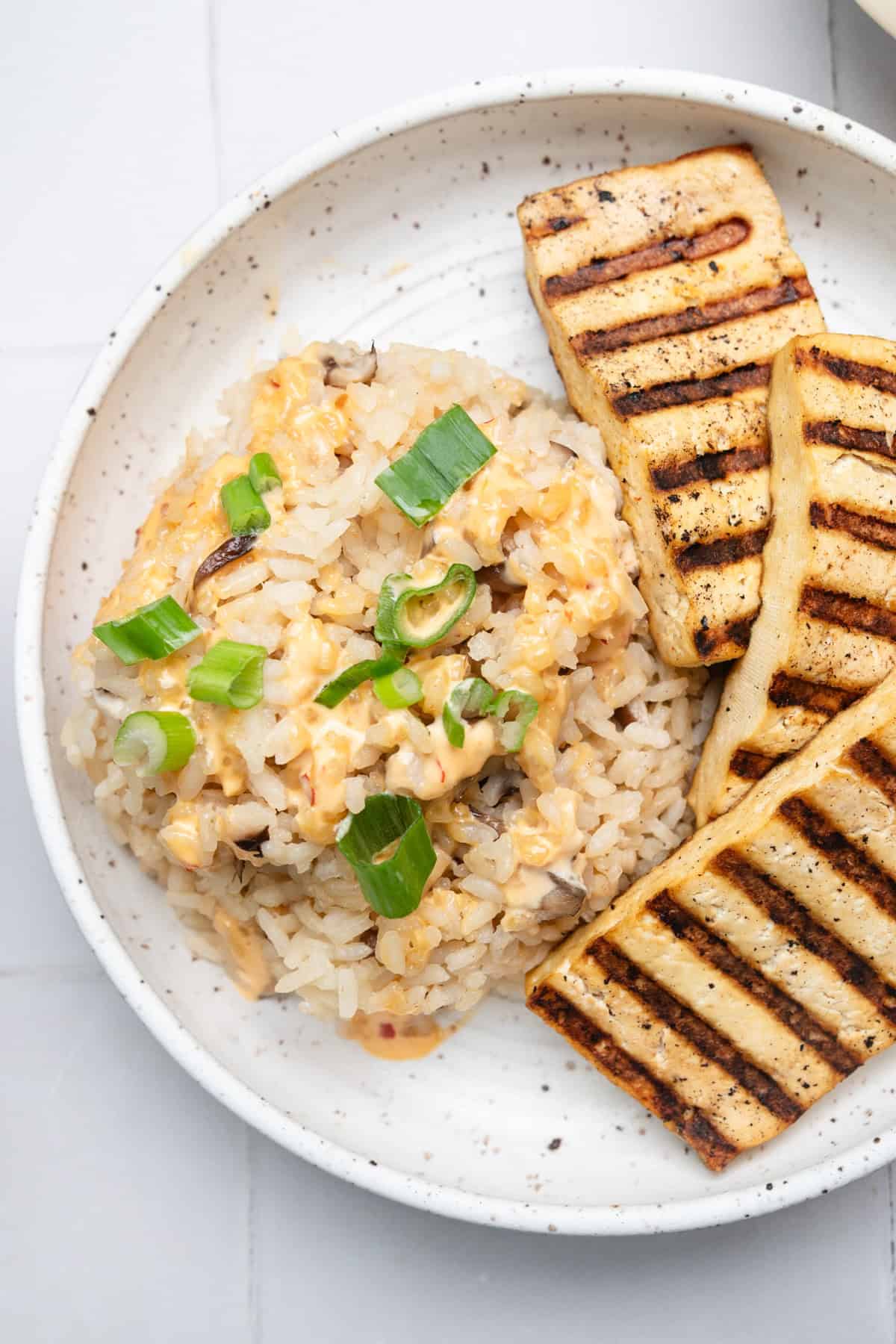 White plate with scoop of rice topped with sliced green onions and three slabs of grilled tofu.