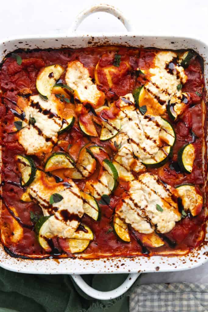 Baked ravioli, ricotta, and zucchini topped with a balsamic drizzle in a white square ceramic baking dish.