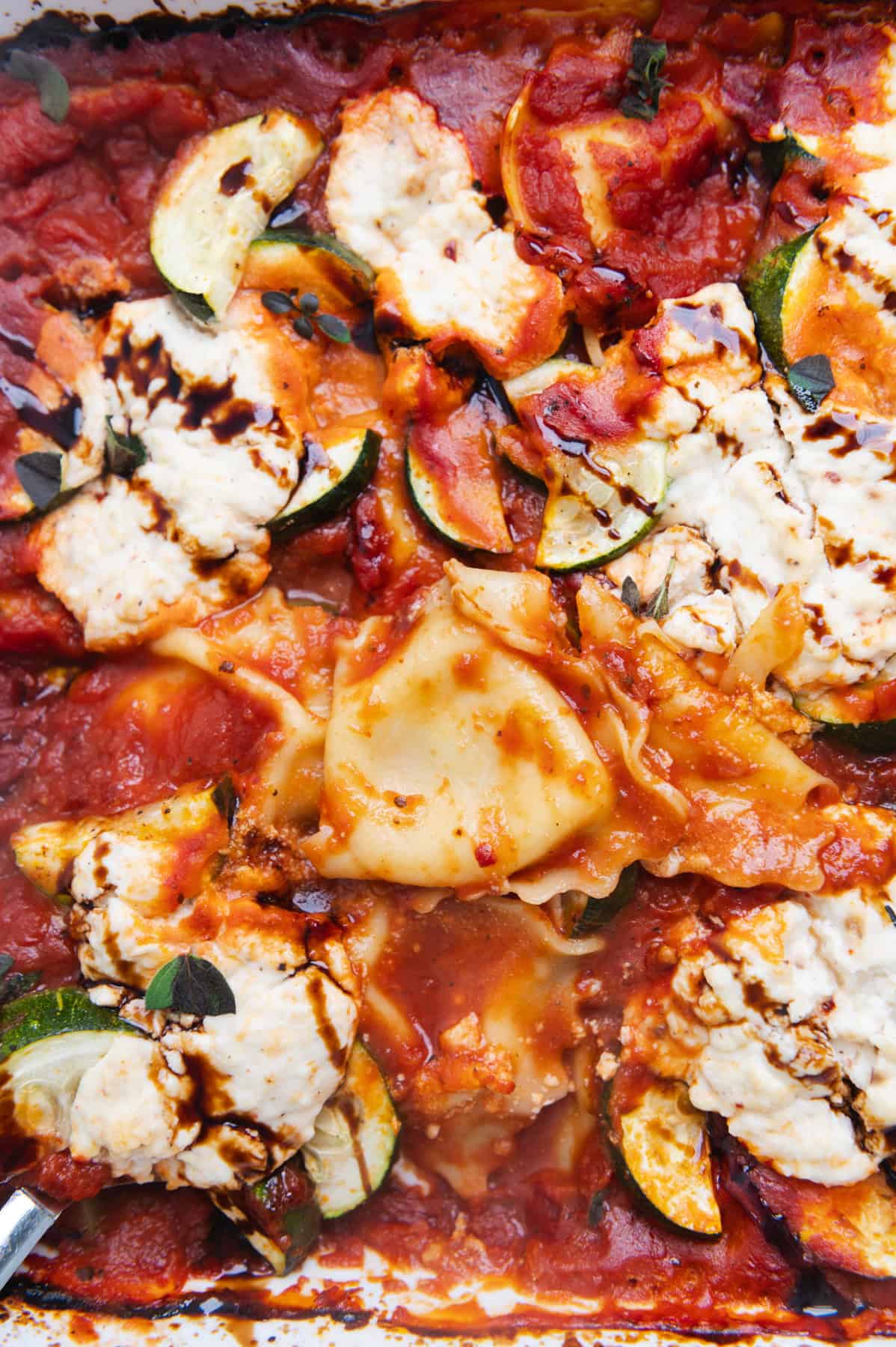 Close up of baked ravioli, ricotta, and zucchini topped with a balsamic drizzle.