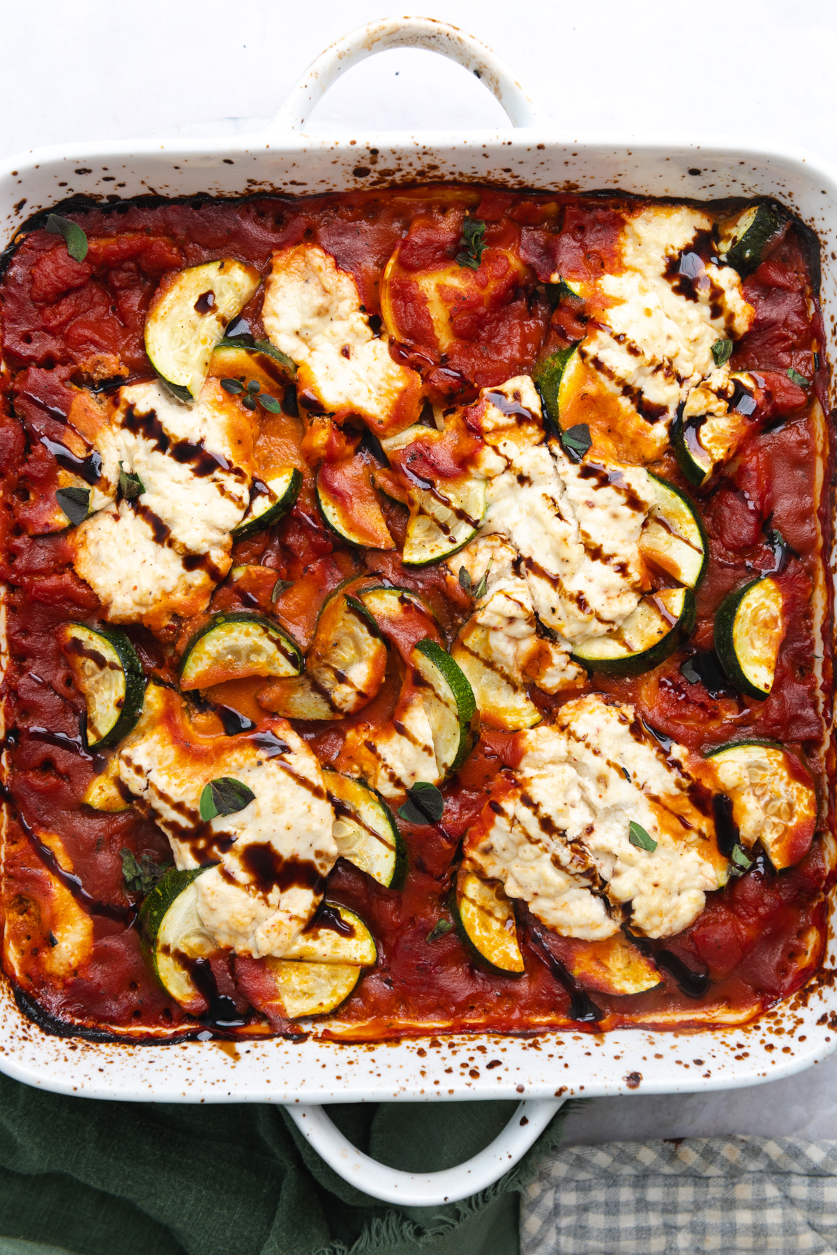 Baked ravioli, ricotta, and zucchini topped with a balsamic drizzle in a white square ceramic baking dish.