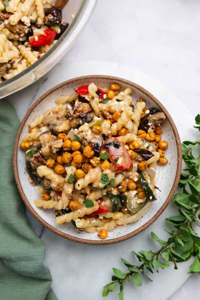 Roasted vegetable pasta salad topped with chickpeas in a brown-rimmed bowl on a marble countertop.