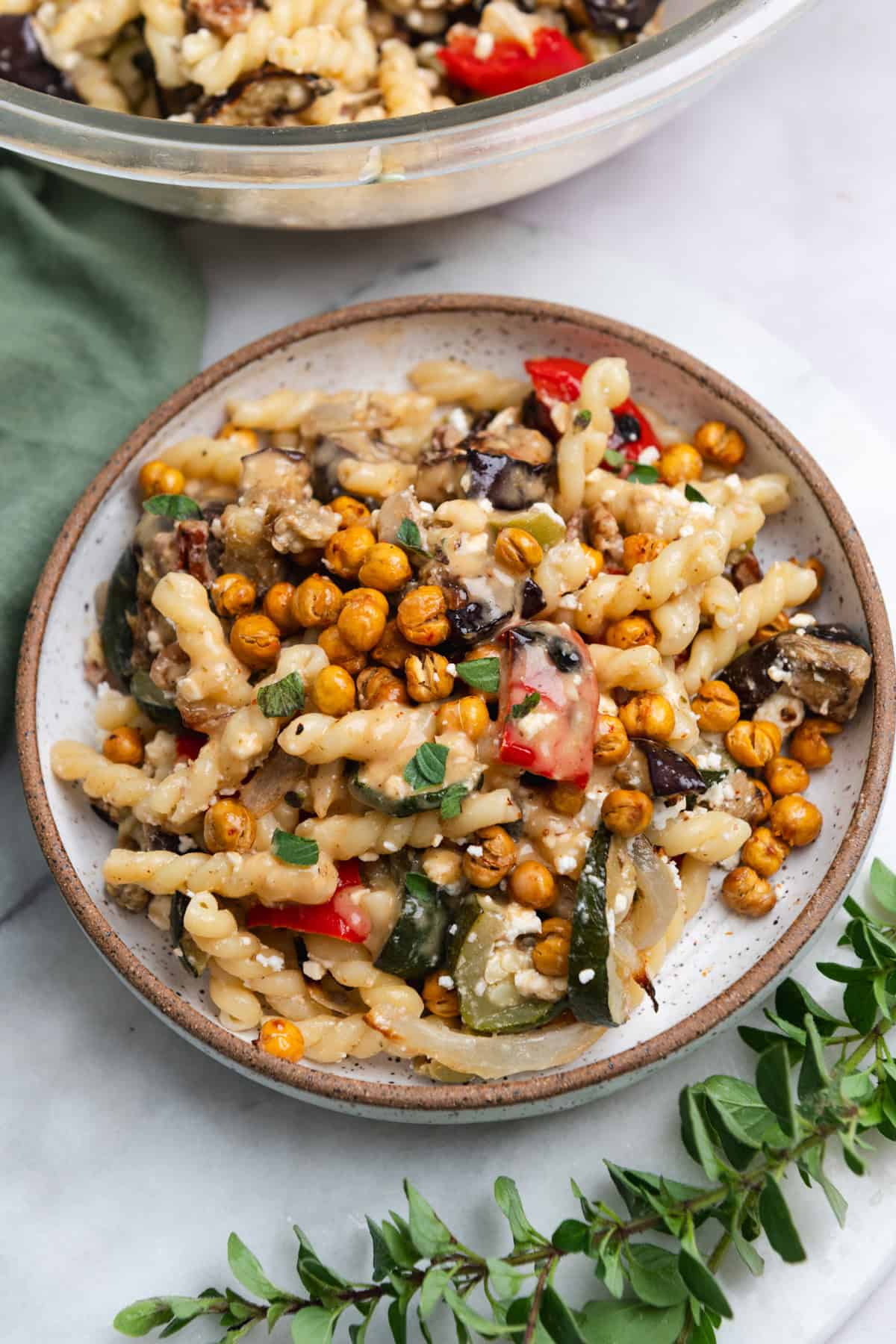 Side view of vegetable pasta salad topped with chickpeas in a brown-rimmed bowl on a marble countertop.