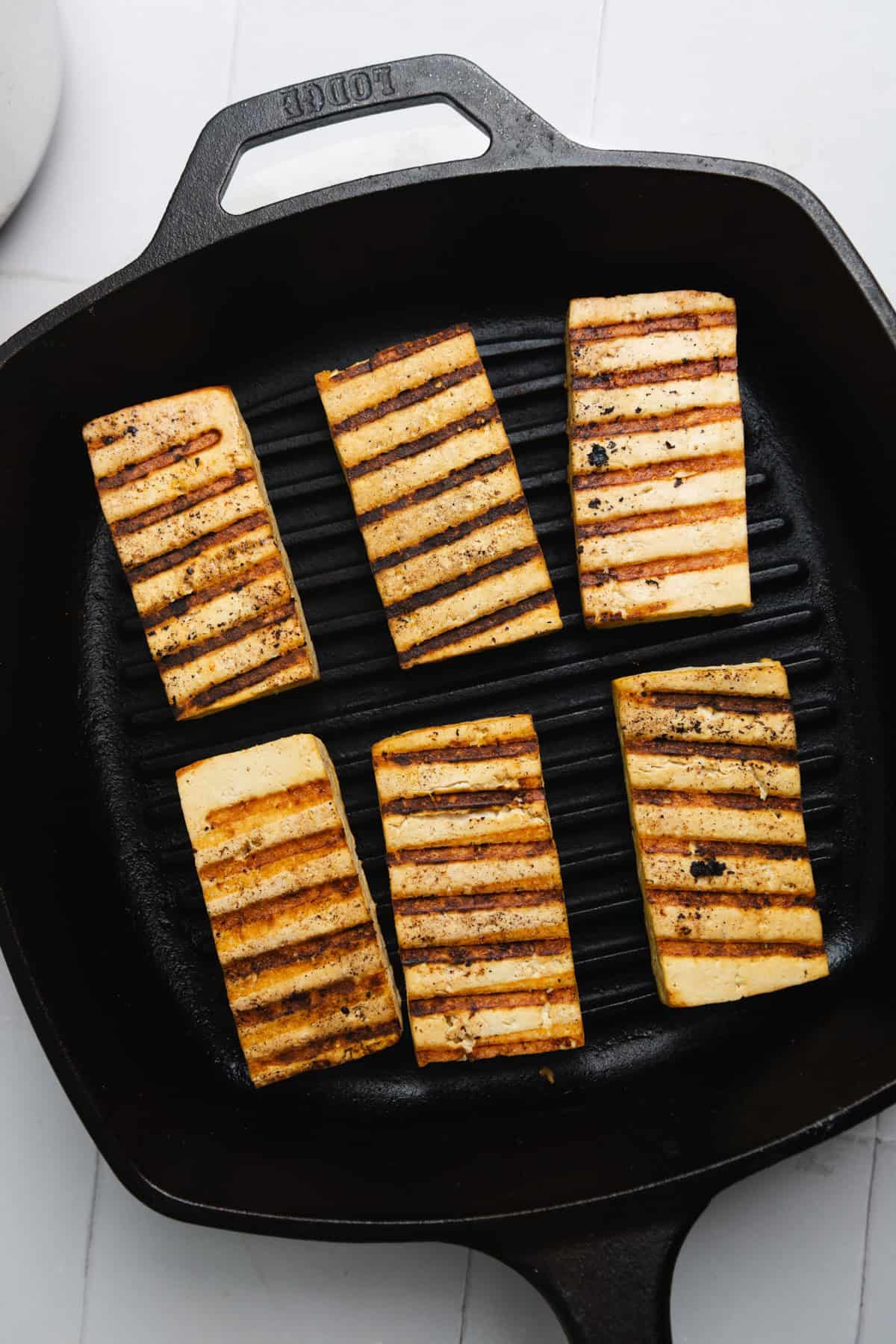 Six pieces of tofu with grill marks on them on a grill pan.