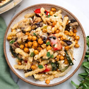 Roasted vegetable pasta salad topped with chickpeas in a brown-rimmed bowl on a marble countertop.