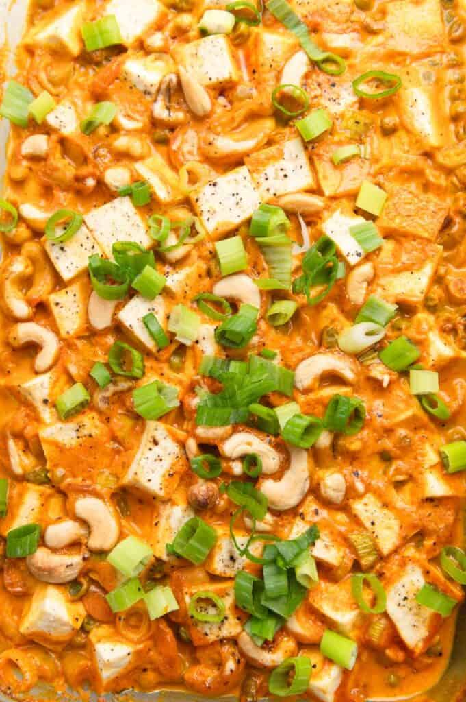 Close up of tofu and cashews in red curry sauce with sliced green onions on top.