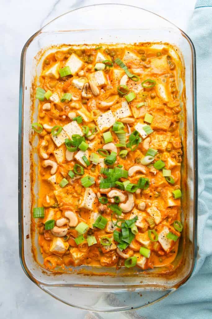 Glass baking dish filled with tofu curry topped with green onions.