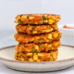 Brown-rimmed white plate with a stack of five corn fritters on it.