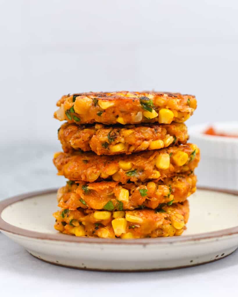 Brown-rimmed white plate with a stack of five corn fritters on it.