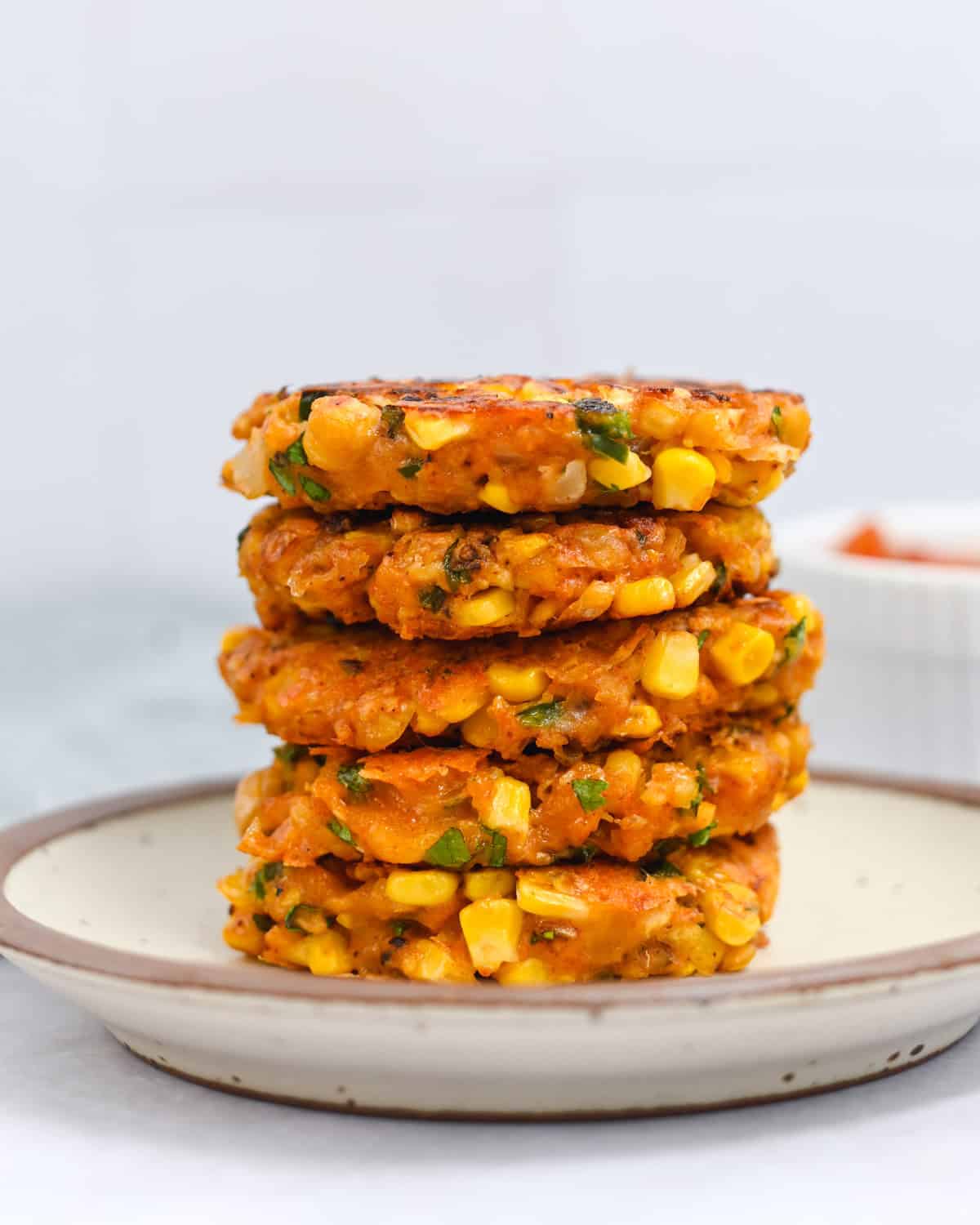 Brown-rimmed white plate with a stack of five corn fritters on it.