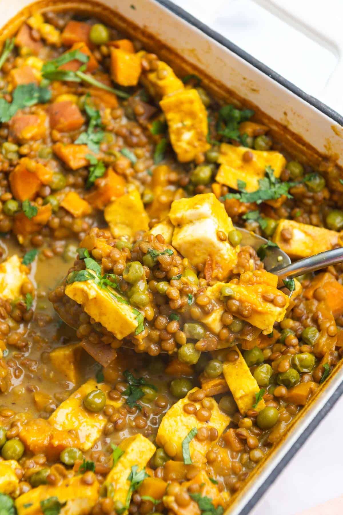 Metal serving spoon lifting a scoop of lentils out of a baking dish.