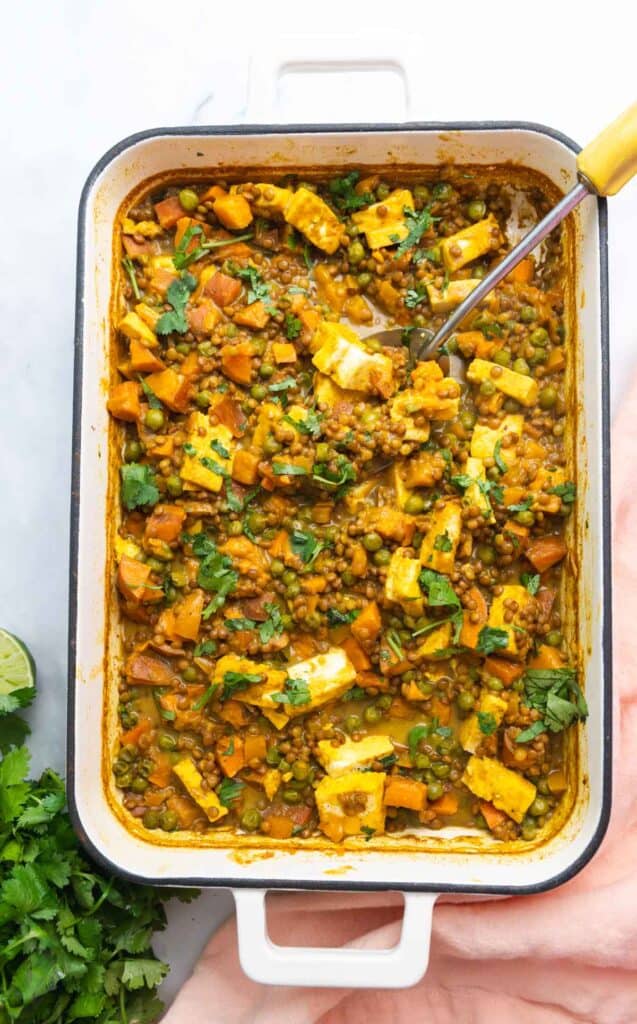 Top down view of white rectangular enamel baking dish filled with lentils, sweet potato, and paneer casserole.