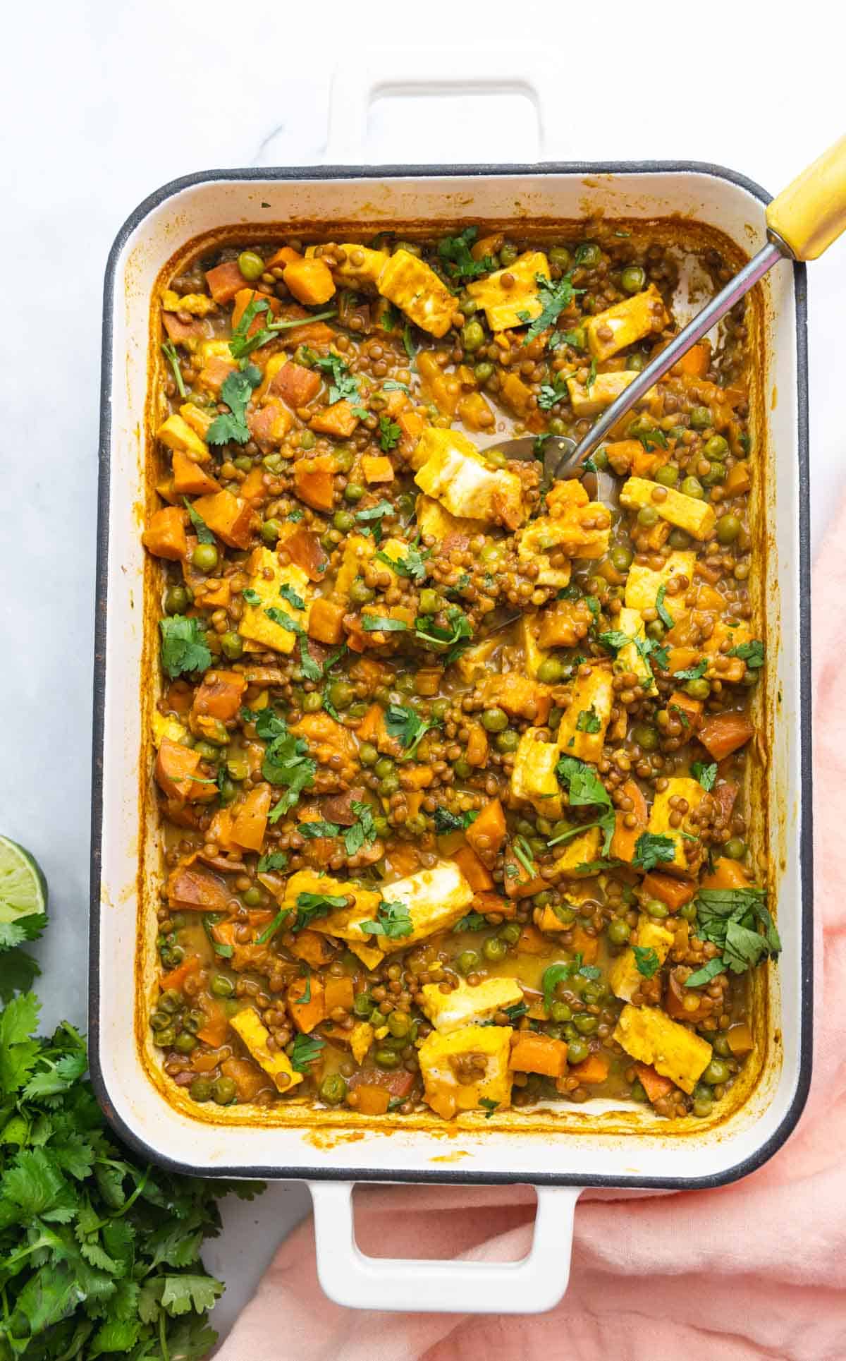 Top down view of white rectangular enamel baking dish filled with lentils, sweet potato, and paneer casserole.
