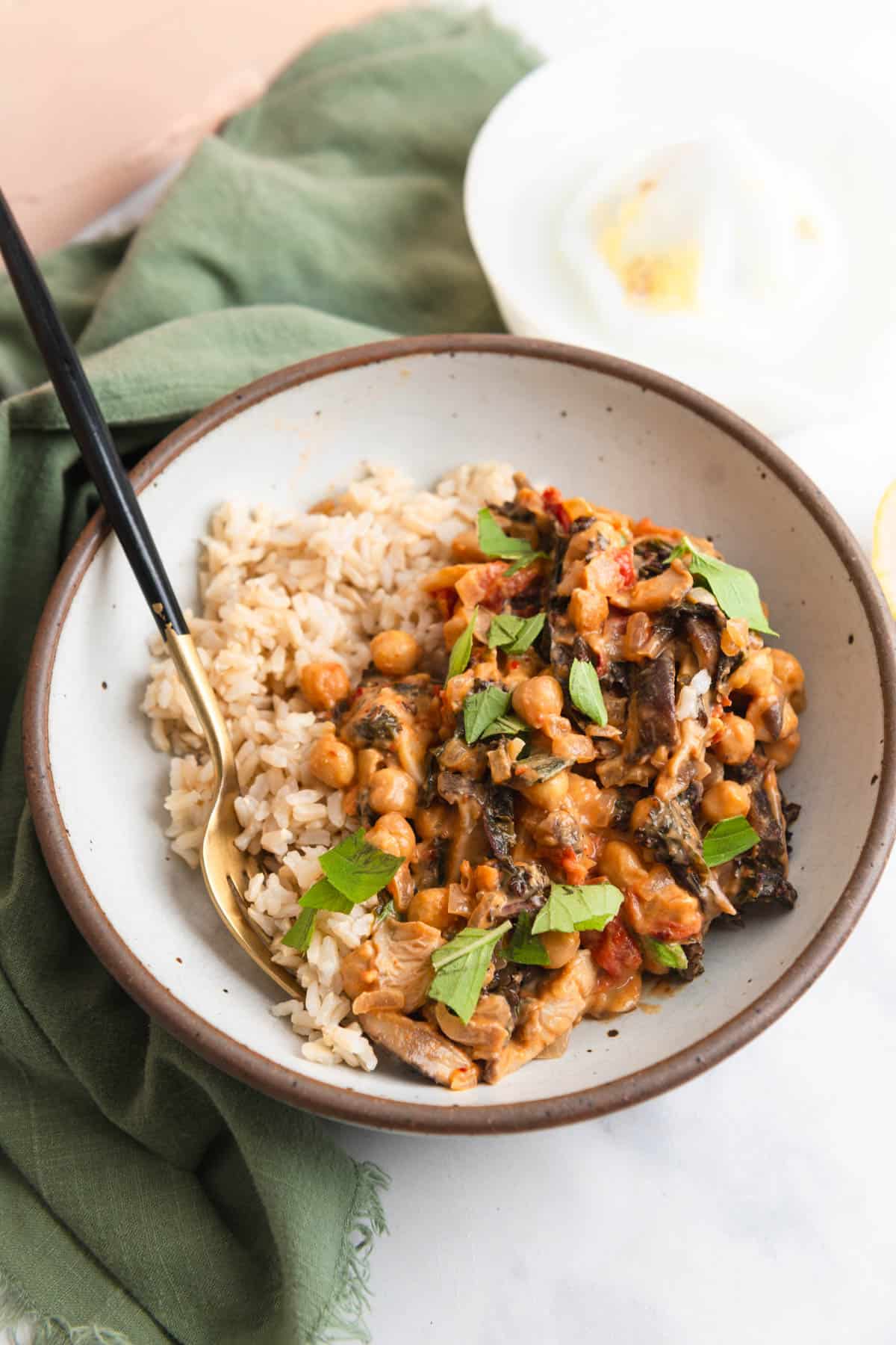 Bowl of miso peanut chickpeas and brown rice on a marble countertop and green cloth.