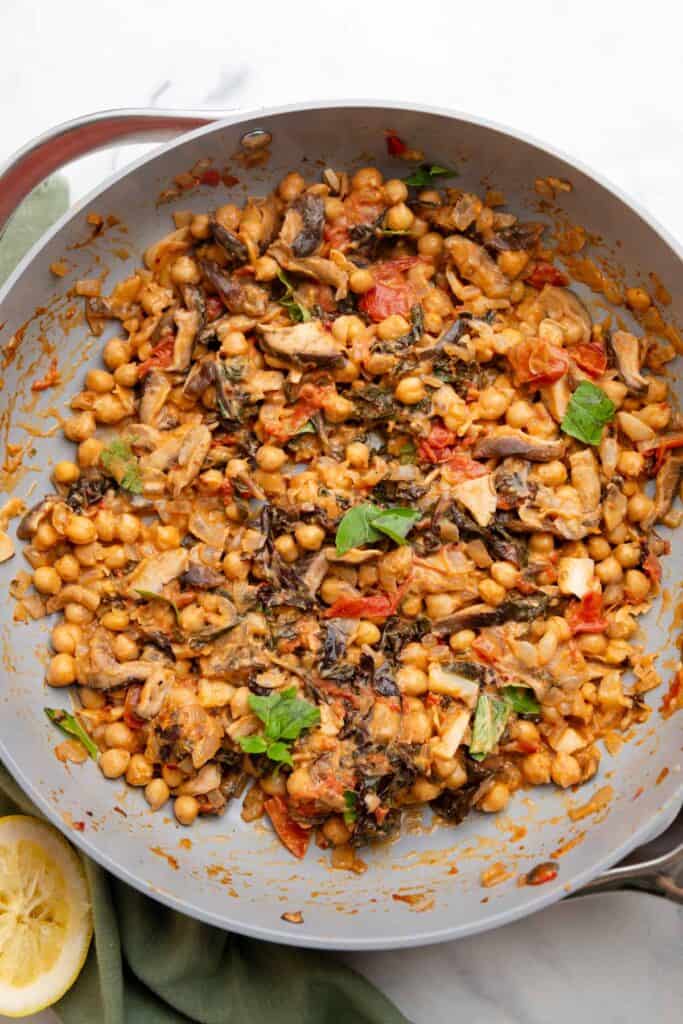 Large gray skillet filled with peanut chickpeas that are topped with leaves of basil.