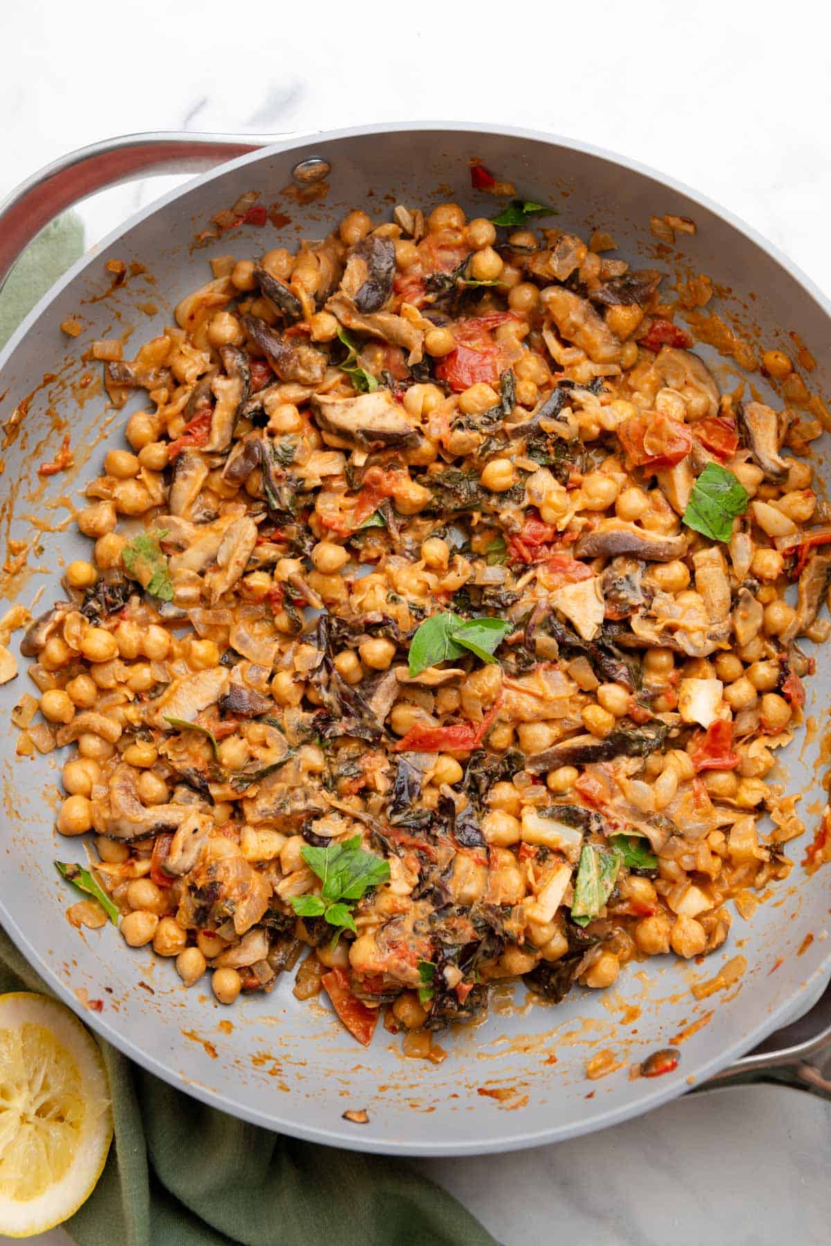 Large gray skillet filled with peanut chickpeas that are topped with leaves of basil.