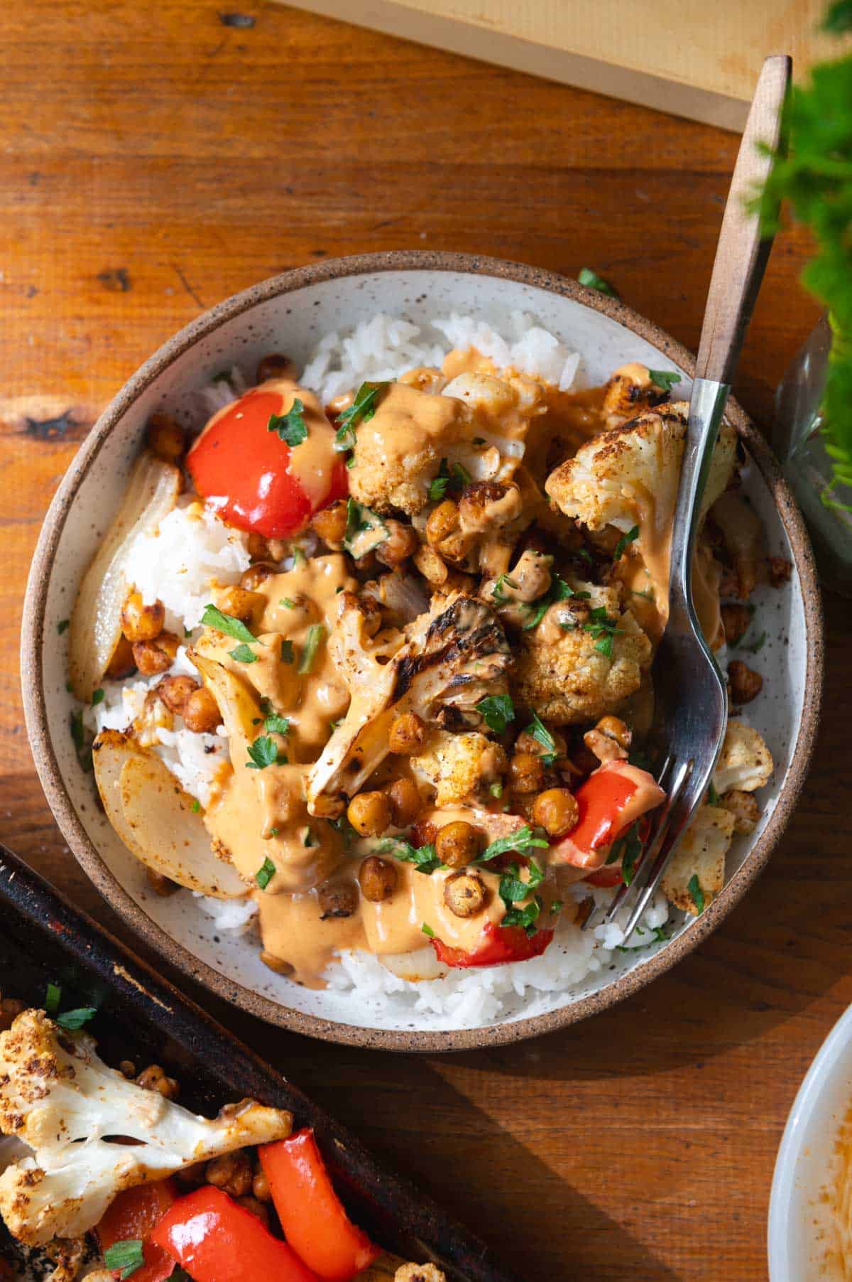 Overhead view of a bowl of rice topped with roasted cauliflower and chickpeas and buffalo sauce.