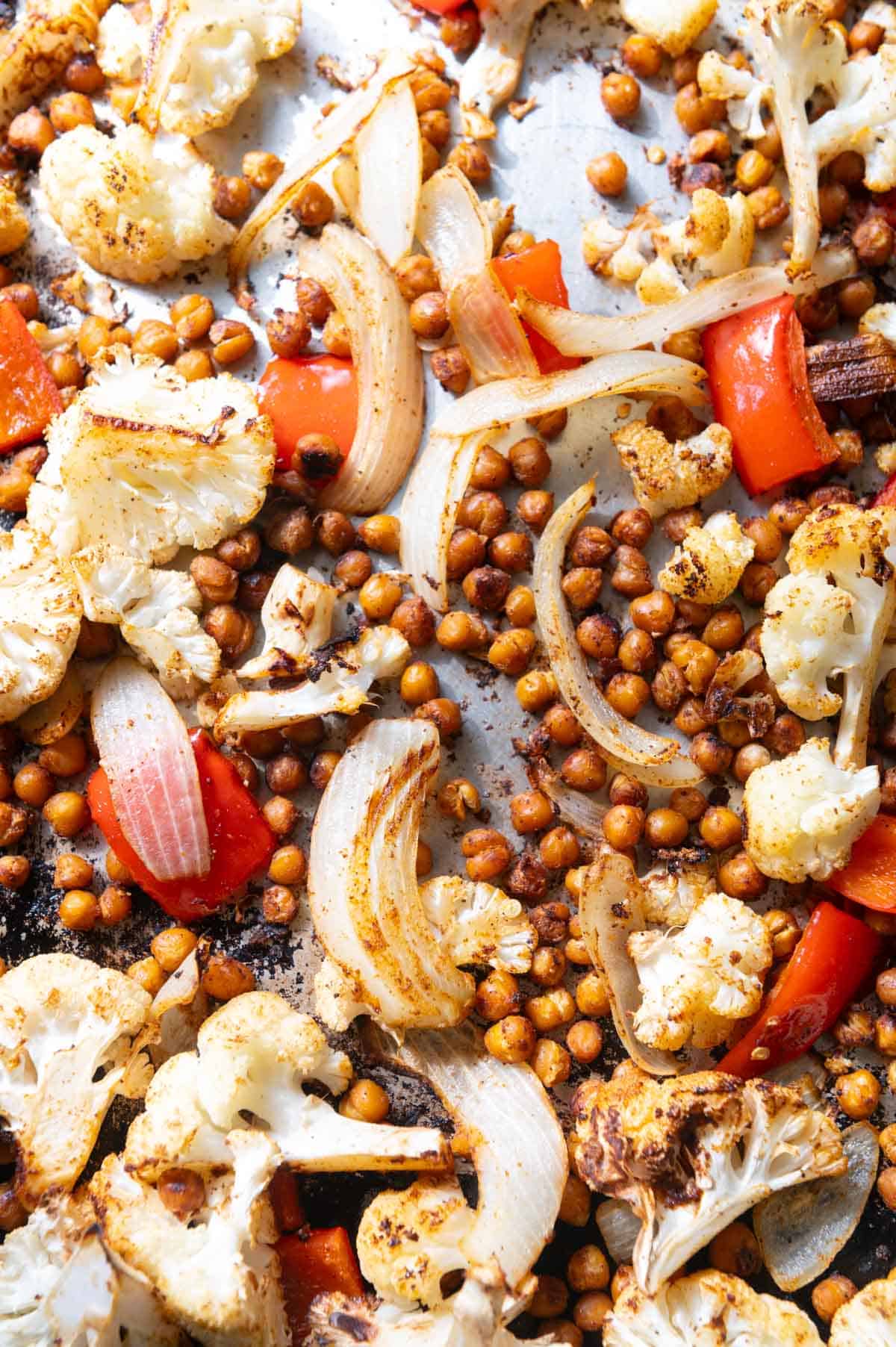 Close up of chickpeas, onion, red pepper, and cauliflower on a sheet pan.