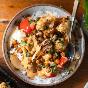 Overhead view of a bowl of rice topped with roasted cauliflower and chickpeas and buffalo sauce.